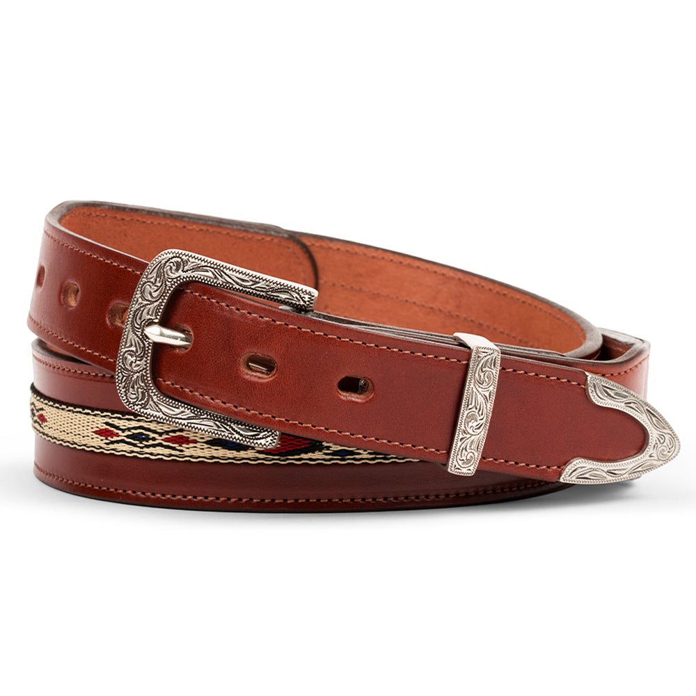 The Seneca Tapered by Hanks Belts in Oak features premium English bridle vegetable-tanned leather, an ornate silver buckle, tip, and loop with intricate engravings, plus a decorative woven section for western style.