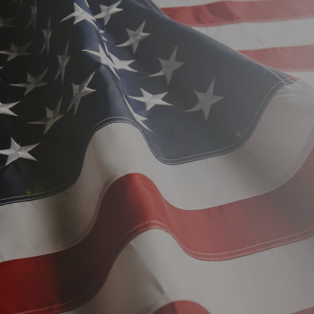 80's. Close-up of an American flag with stars and stripes. Text below the image: A challenging time for retailers as the market is flooded with cheap imports from around the world. Although tempting as it may have been, Hank kept his eye and focus on quality and service. Products made in the USA meant a lot and was truly the cornerstone of the business.