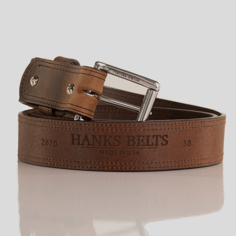 2001. Brown leather belt with silver buckle on a reflective surface Text below the image: “Hank’s Belts” website makes its first debut. Starting out with our best colors, it has grown to offer numerous styles and colors. Focus is kept on the design and manufacturing of all belts made in the USA.