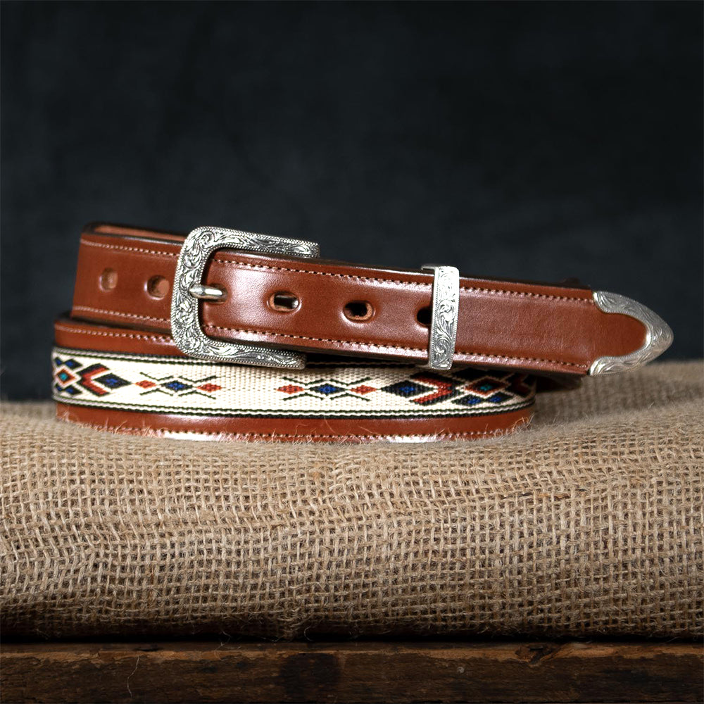 The Seneca Tapered by Hanks Belts, crafted from premium English Bridle leather with red-black-tan stitching, showcases a western-style engraved silver buckle and tip, coiled on burlap with a dark backdrop.