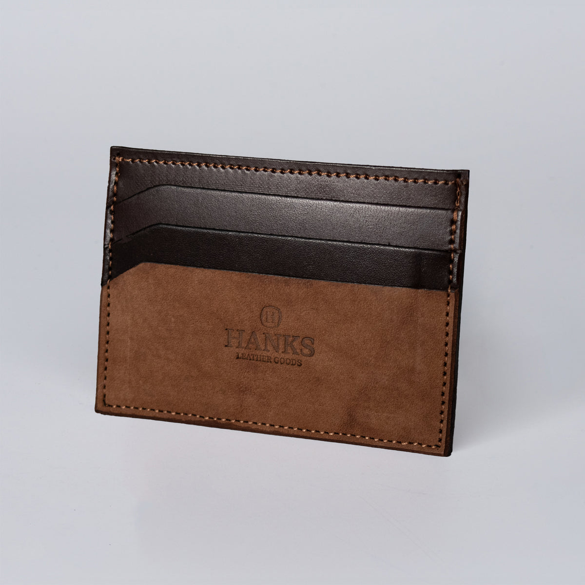 The Whiskeytown Cardholder by Hanks Belts, a brown and dark leather wallet, stands upright against a plain light background with the brand name embossed on the front.