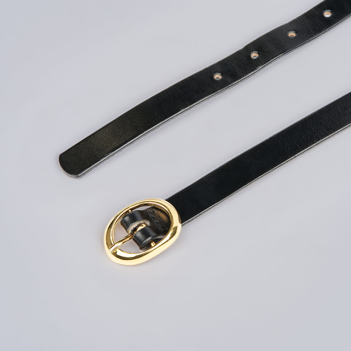 The Ivy by Hanks Belts is a black leather belt with a shiny gold oval buckle, shown laid flat on a light gray background. Multiple adjustment holes are visible.