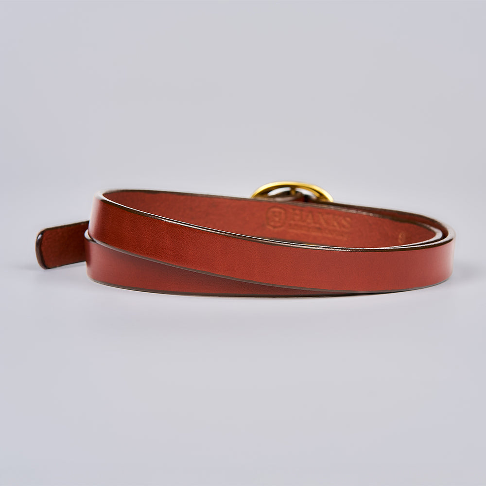 The Ivy by Hanks Belts, a brown leather belt with a gold buckle, is coiled neatly on a light grey background.