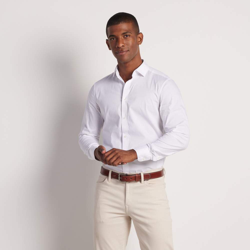 A man with short hair and a neutral expression adjusts his cuff while wearing a white shirt, beige pants, and The Highland Lined belt by Hanks Belts against a plain white background.
