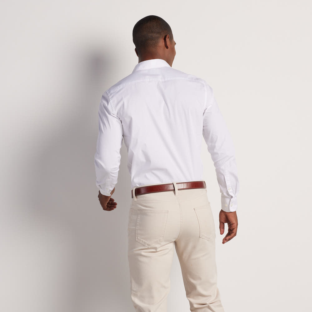 A man stands with his back to the camera, wearing a white shirt, beige pants, and The Highland Lined belt from Hanks Belts—crafted from vegetable-tanned leather—against a plain light background.