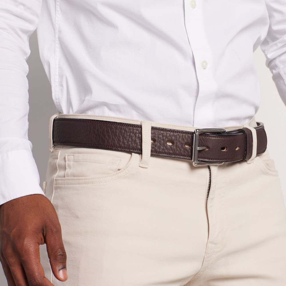 A person wears a white button-up shirt with light beige pants, finished with Hanks Belts' The Tuscan Embossed Lined premium leather belt featuring a stainless steel buckle.