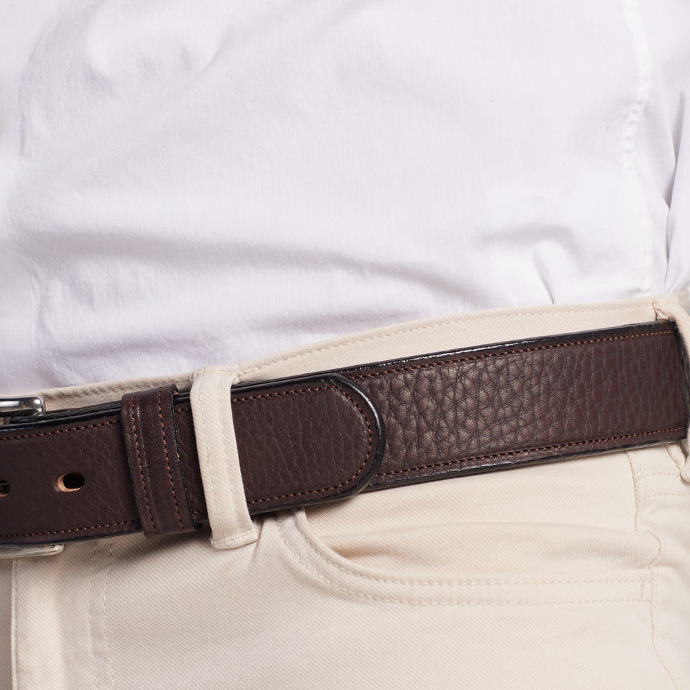 A close-up of a person wearing a white shirt tucked into beige pants, secured with Hanks Belts’ The Tuscan Embossed Lined—a premium leather belt with a textured dark brown strap and stainless steel buckle.