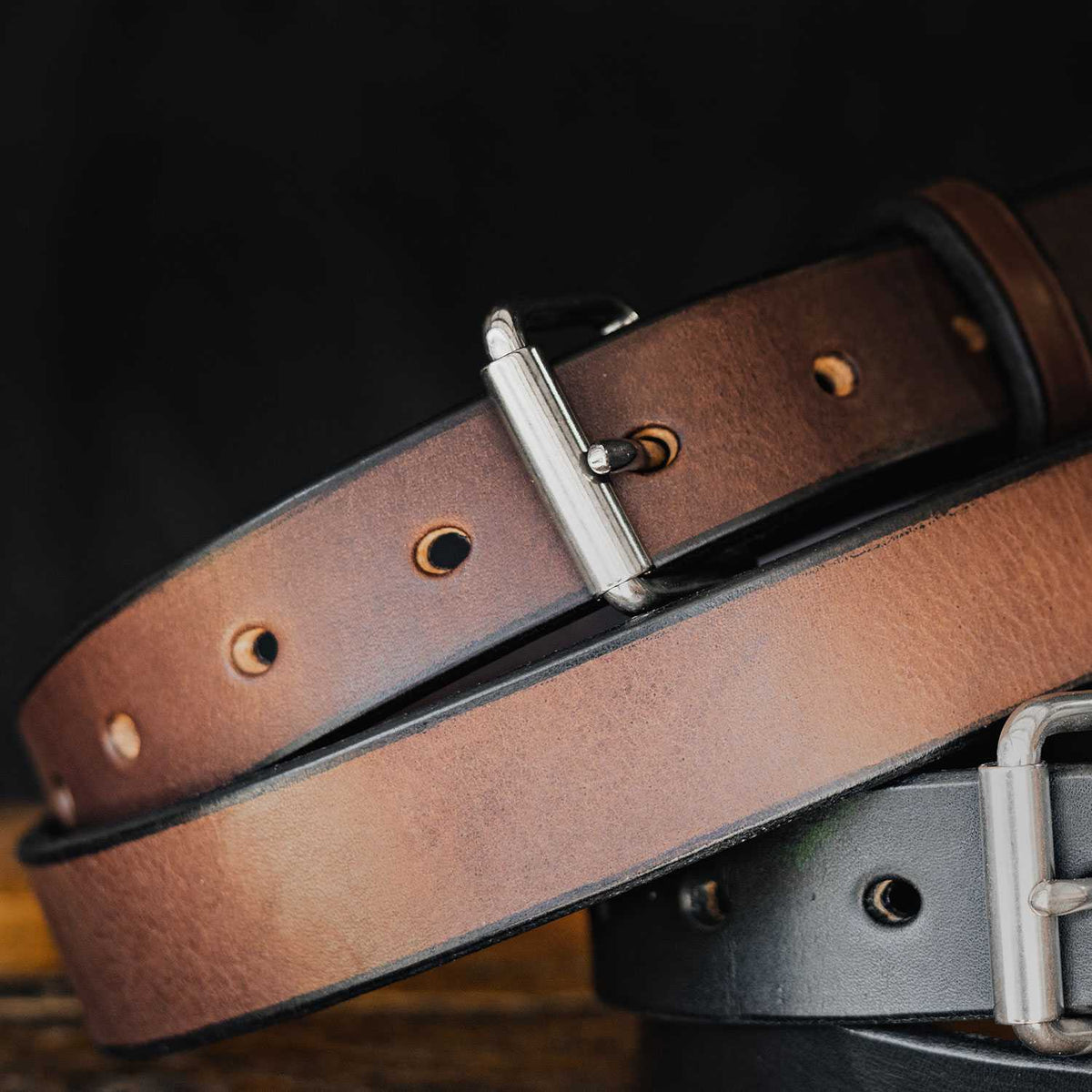Close-up of Hanks Belts' The Deputy: a brown leather belt layered atop a black concealed carry belt, both with silver buckles, displayed against a dark background.
