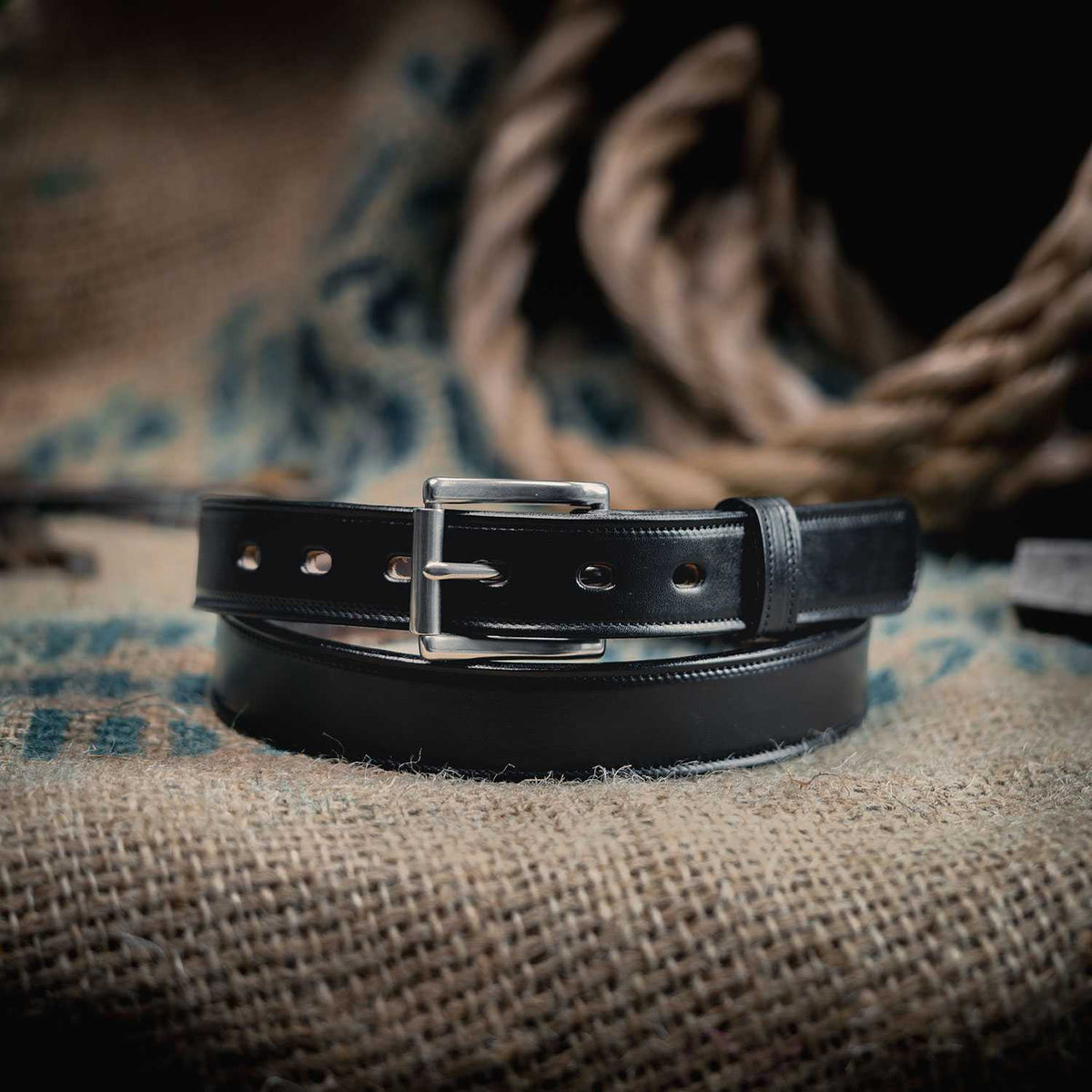 The Highland Lined by Hanks Belts, made from English bridle leather and finished with a silver buckle, is coiled on burlap among thick ropes for a rustic look.