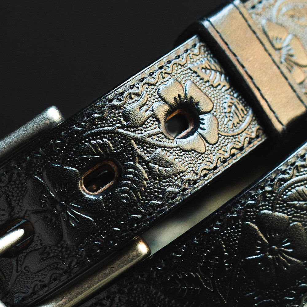 Close-up of The Floral Embossed by Hanks Belts, a full-grain leather belt with intricate floral embossing and a shiny silver buckle. Made in the USA, this belt highlights exceptional craftsmanship and texture.