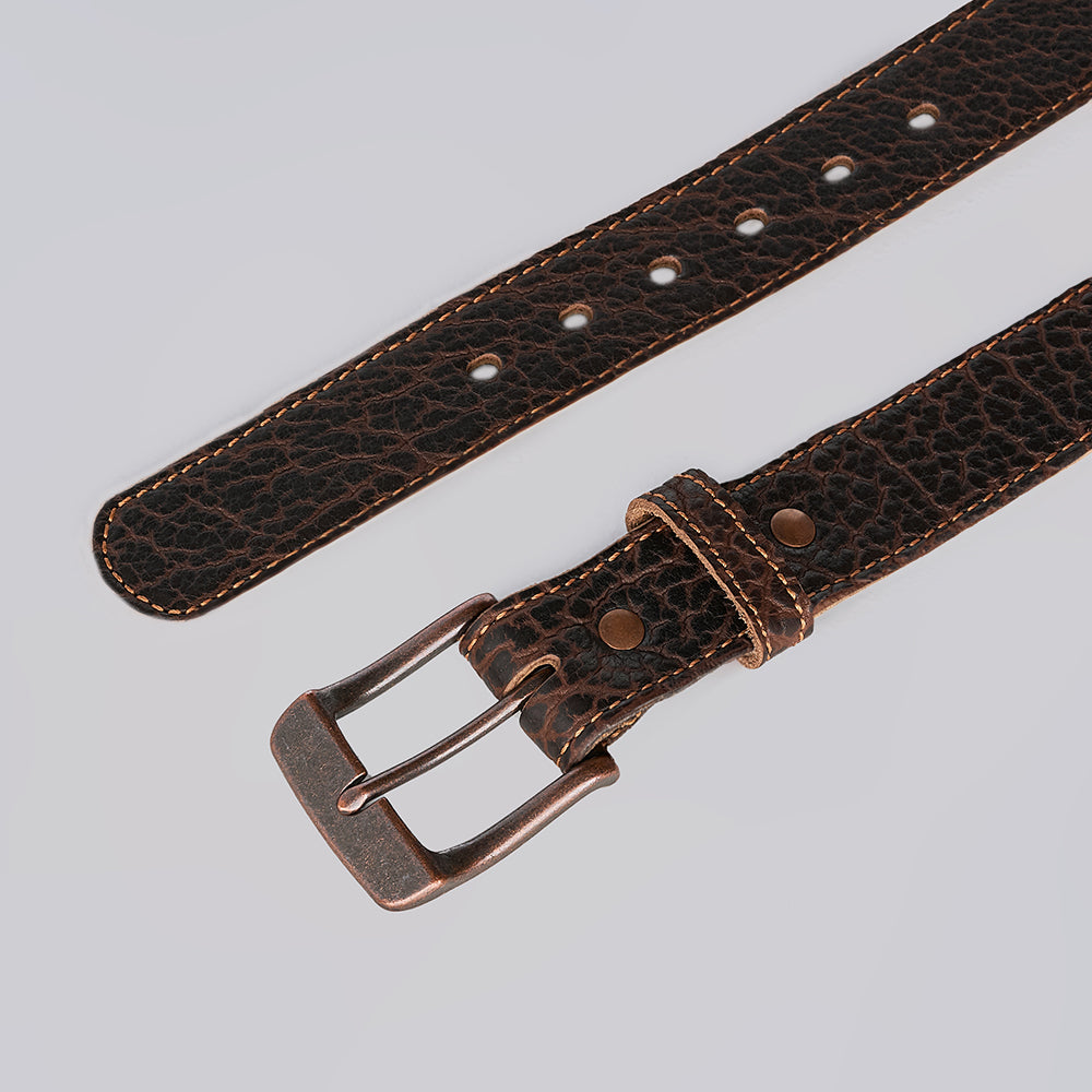 A close-up of The Yellowstone by Hanks Belts, a rugged leather belt with textured surface, visible stitching, and a metallic buckle, displayed on a neutral light background.