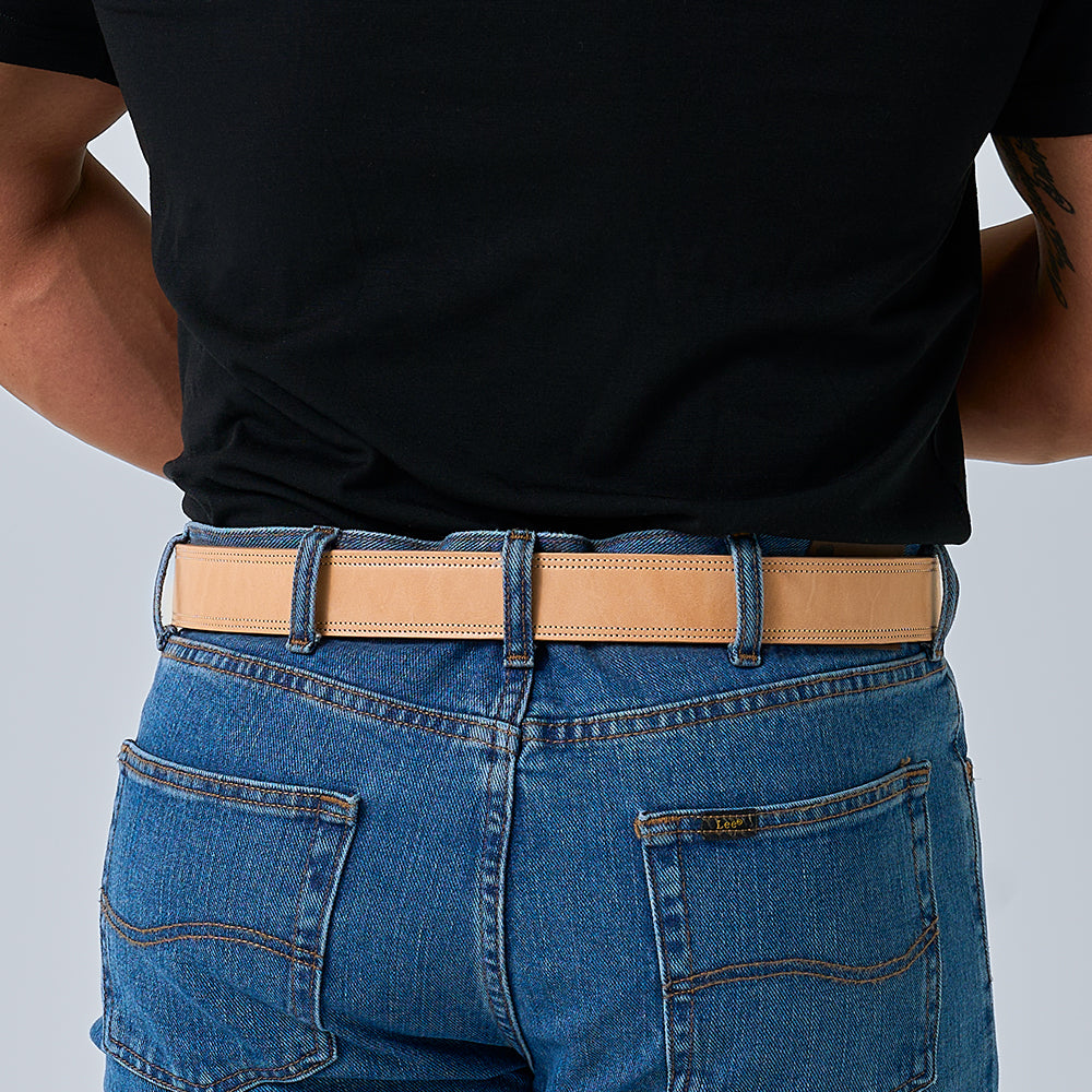 A person in a black shirt tucked into blue jeans, seen from the back, wears Hanks Belts' The Premier Double Layer—a tan English bridle belt crafted from vegetable-tanned leather.