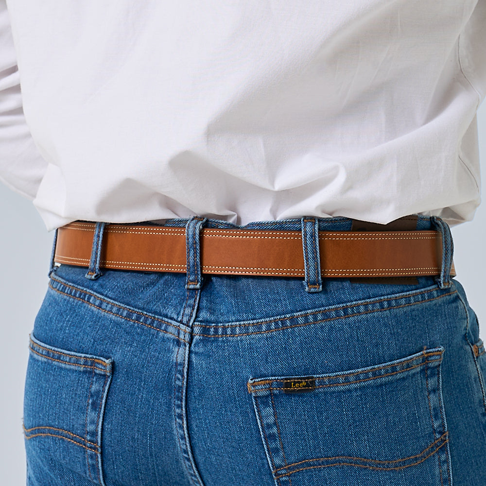 A person is shown from the back wearing blue denim jeans, a white shirt tucked in, and "The Premier Double Layer" leather belt by Hanks Belts; the jeans have visible stitching, belt loops, and a "Lee" brand label on the pocket.