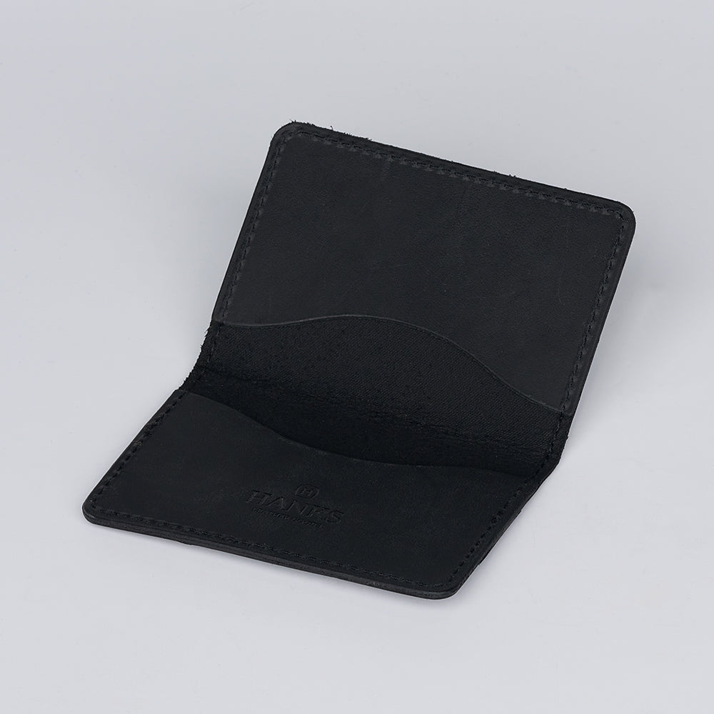 The Hanks Belts Tupper Bifold Card Holder, crafted in black leather, is open to display its two inner pockets. This ultra-thin wallet is set against a plain light gray background.