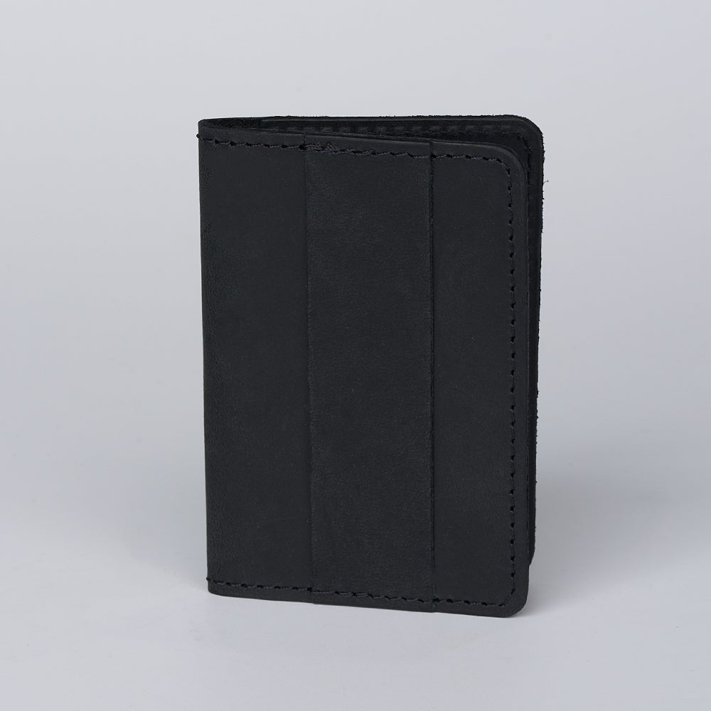 The Hanks Belts Tupper Bifold Card Holder, a black ultra-thin leather wallet with visible edge stitching and a minimalist design, stands upright on a plain light gray background.