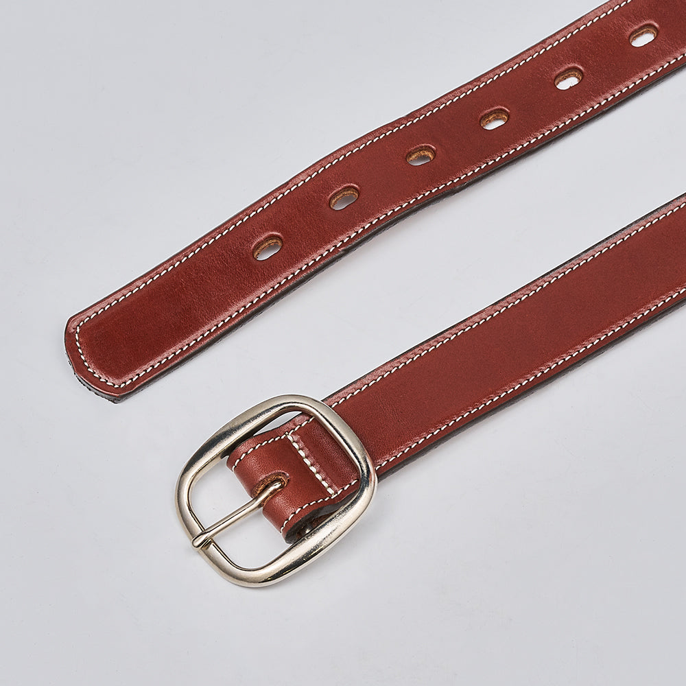 The Eloise by Hanks Belts, a women's vegetable-tanned brown leather belt with white stitching and a silver buckle, made in the USA, is laid flat on a light gray surface.