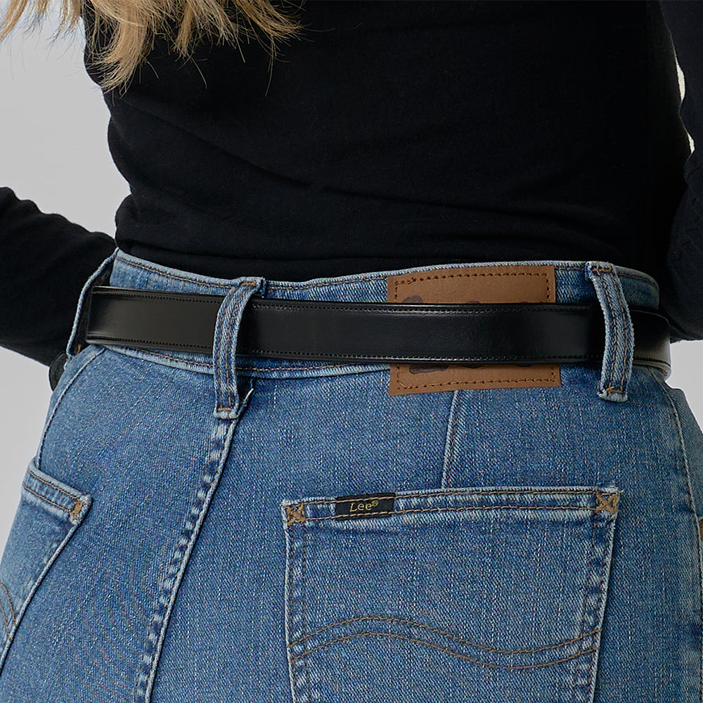 A person shown from the back waist down wears blue Lee jeans with a brown patch, a black long-sleeve top, and the Addyson - 1" black belt by Hanks Belts with a brass buckle.
