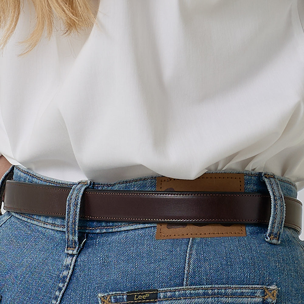 A person wears a white shirt tucked into blue jeans, highlighted by the Addyson - 1" classic leather belt from Hanks Belts with a brass buckle; the image focuses on the waist and part of the outfit.