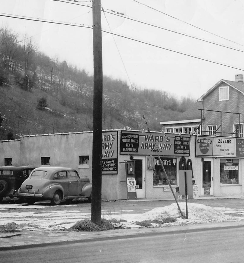 1949 .Vintage black and white photo of a small town street with a store named 'Ward's Army Navy'. Text below the image: A young Hank reports to work for a newly opened Army & Navy store located in Binghamton, NY. Common at the time, A&N stores supplied the public with quality goods from surplus which was generated by the military. 