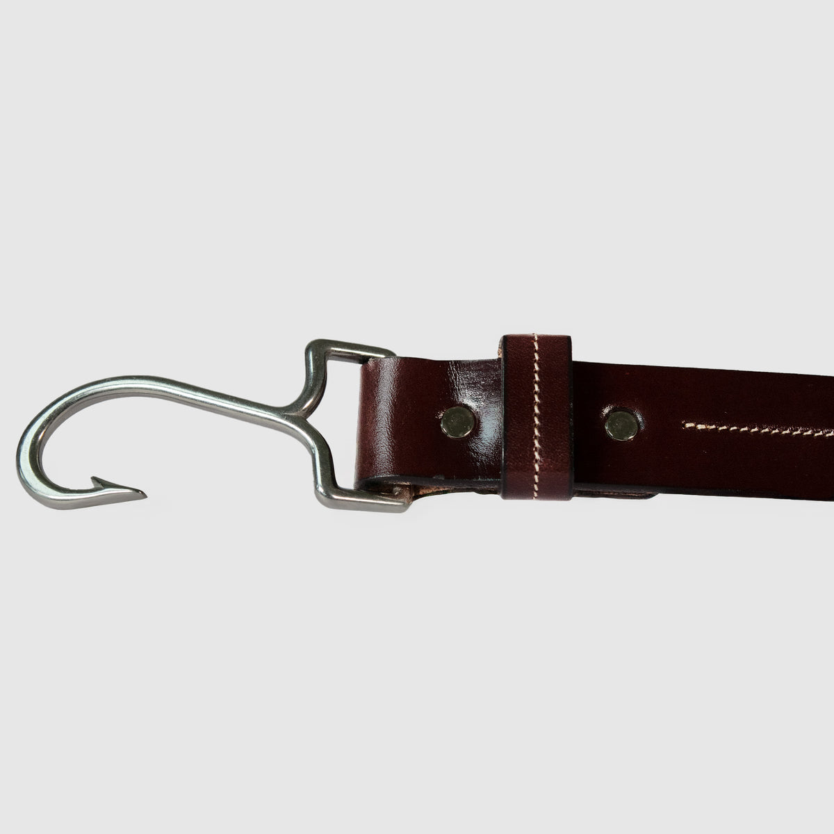 A close-up of The Castaway - Limited Edition by Hanks Belts, made from Havana English Bridle leather with a metal hook on one end, set against a plain light gray background.