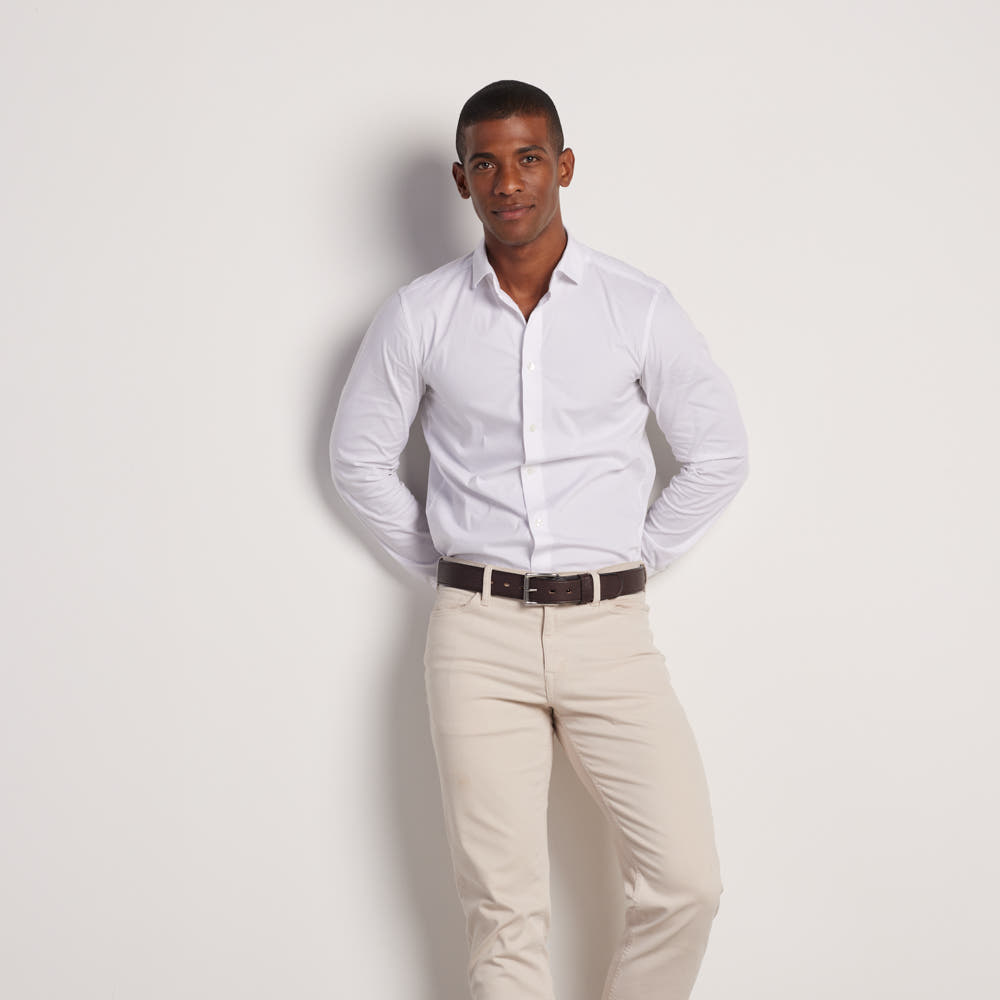 A man stands against a white background, wearing a white shirt tucked into beige pants with The Tuscan Embossed Lined premium leather belt by Hanks Belts, featuring a stainless steel buckle. He looks at the camera, hands behind his back.